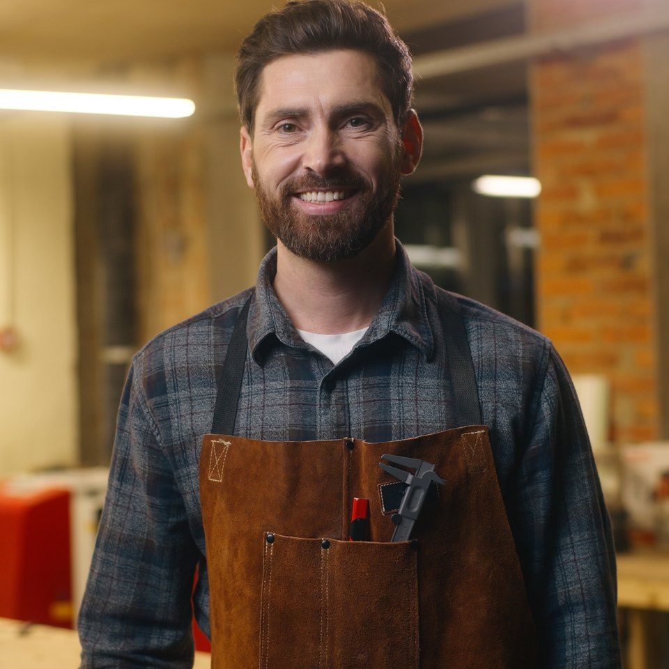 A smiling business owner in a leather apron in his workshop