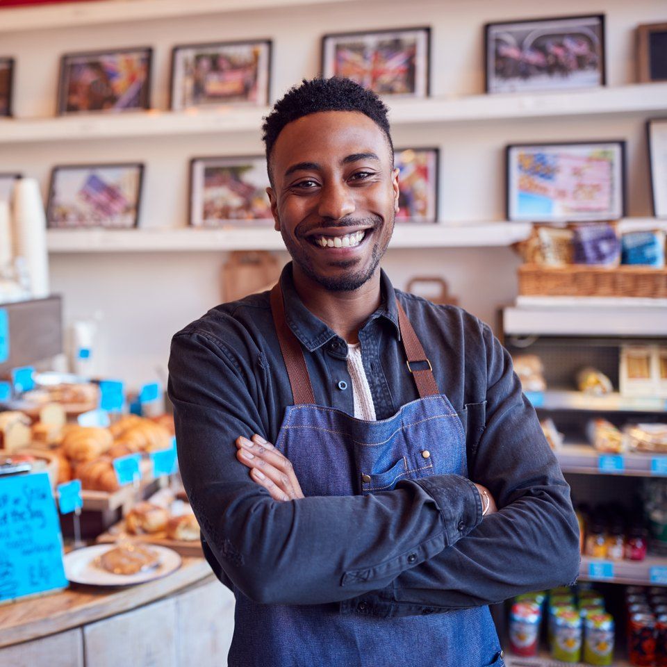 A smiling café owner in a denim apron standing by the counter of his café